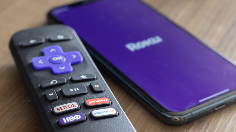 A Roku TV remote placed alongside a smartphone displaying the Roku logo