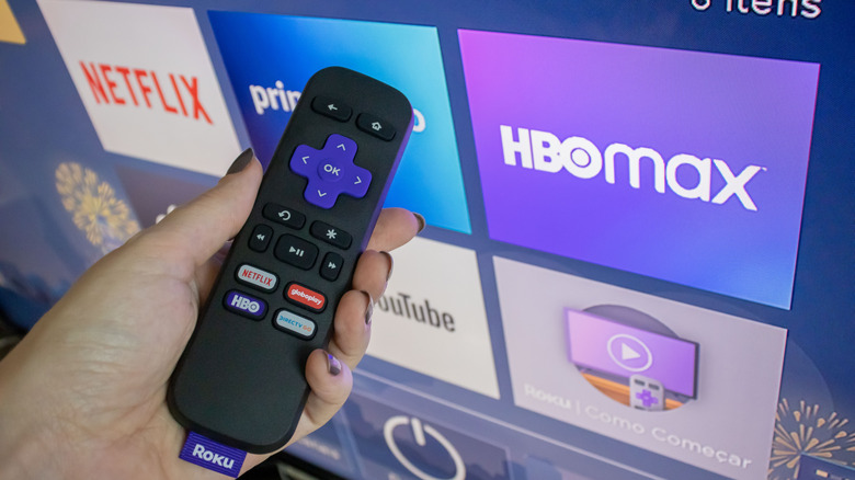 hand holds a roku remote in front of a roku tv homescreen
