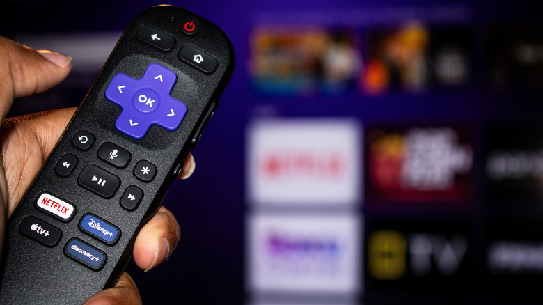 man holds Roku TV remote, menu visible in the background