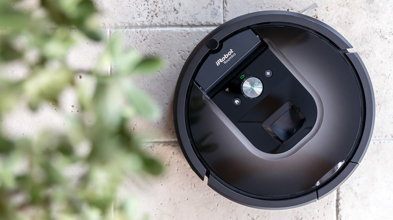 A roomba cleaning a stone tile floor with a plant in the foreground