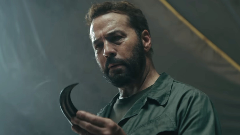 Jeremy Piven looks worried holding a large dinosaur claw  in his hand
