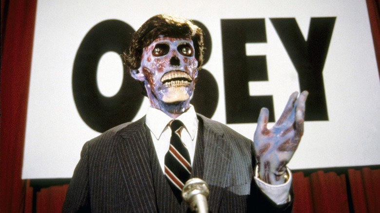 An alien standing on a podium in front of an "Obey" sign in "They Live."