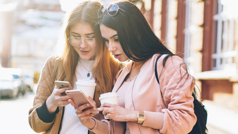 Two young women on the street looking at their phones.