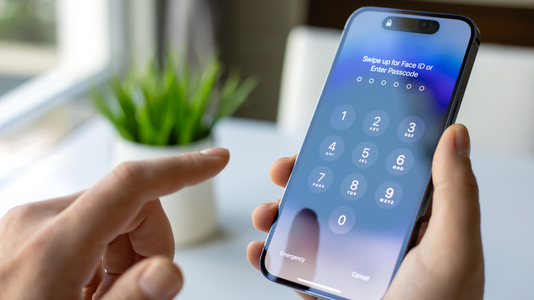 A man holding an iPhone showing the lock screen for Face ID or passcode.