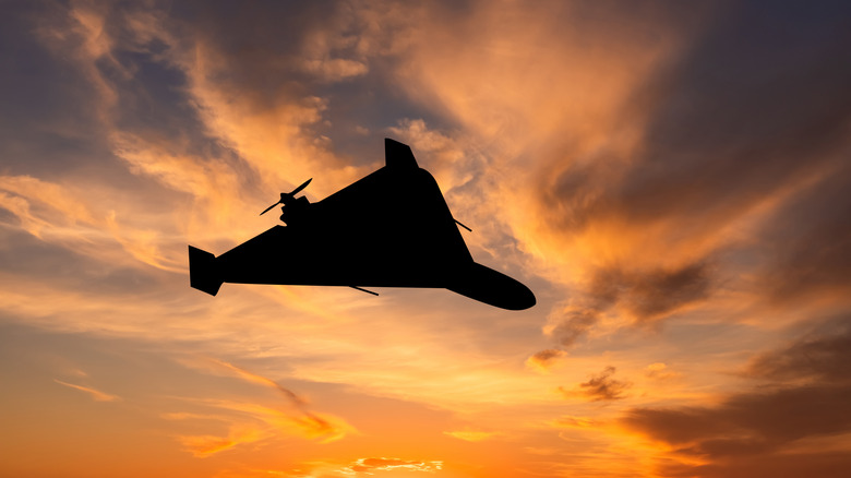 a military grade drone flying in front of a sunset
