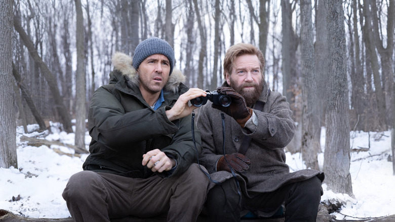 Troy and Nikolai on a stakeout, holding a binocular in the woods