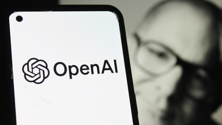 ChatGPT and OpenAI logos on an iPhone with a blurry photo of Jony Ive in the background