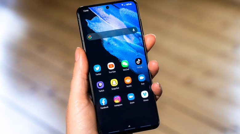 Close-up on a person holding a Samsung Galaxy smart phone, showing the home screen.