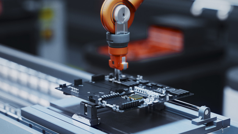 A robotic arm manufactures a motherboard on an assembly line