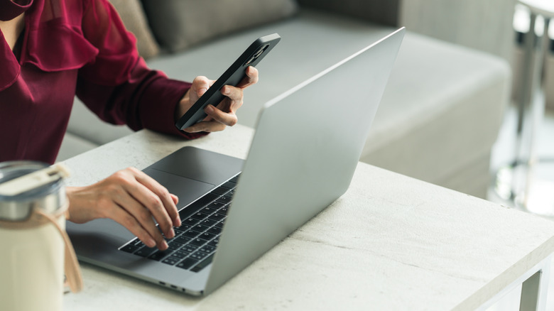 a person holding up a smartphone next to a laptop