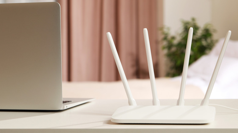 A white wi-fi router placed on a table next to a laptop