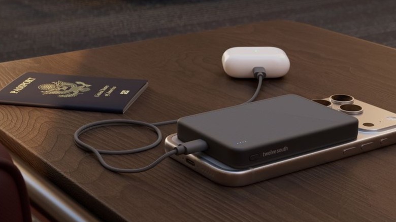 Twelve South's PowerCapsule 10,000mAh MagSafe charger charging an iPhone and AirPods. There's also a U.S. passport on a table.