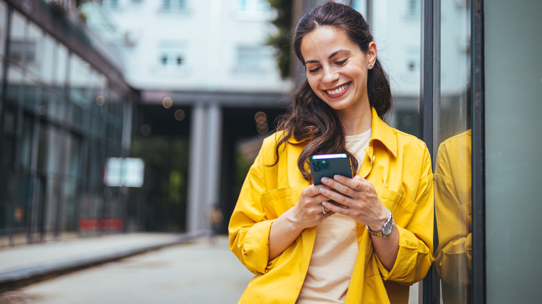 a woman smiling and texting on her phone outside of a building