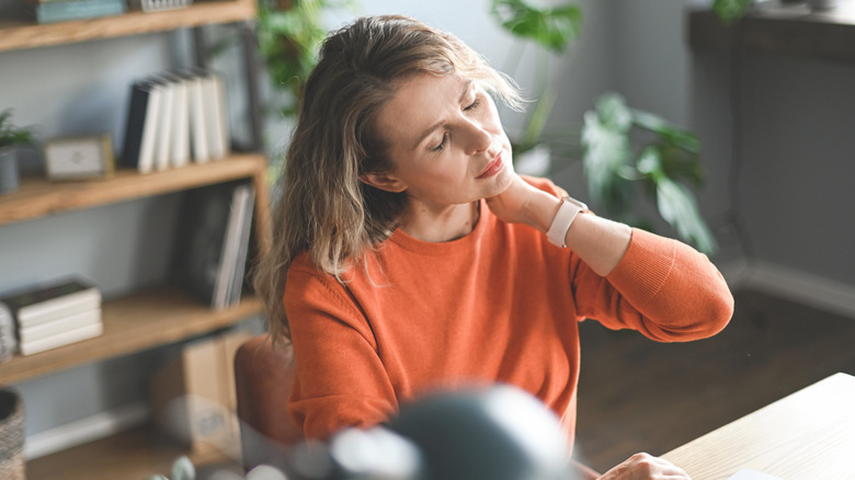 A woman experiencing neck pain at a computer desk.