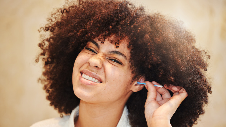 a woman cringing as she uses a Q-Tip in her ear