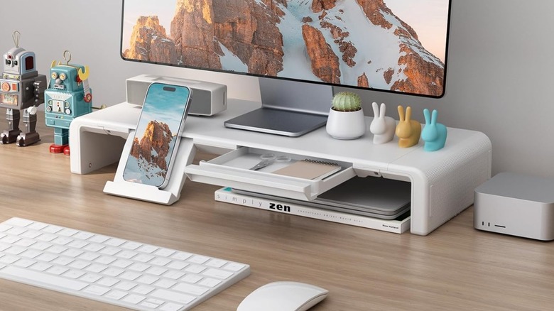 A promotional photo for the Klearlook Adjustable Monitor Stand; the image showcases the stand's compartments, as well as its ability to store items underneath the stand in a real-world application.