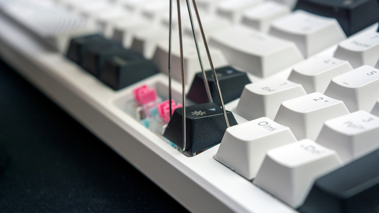 A keycap puller grabbing a key off a white keyboard white with white and black keys.