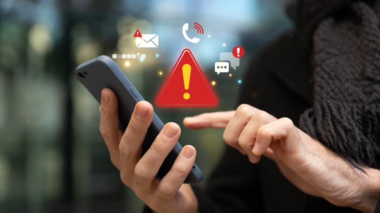 Person holding a smartphone with scam warning icons floating above the screen