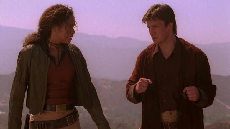 Gina Torres and Nathan Fillion in a scene from "Firefly," the two characters appear to be standing on the top of a hill, with several other hills behind them
