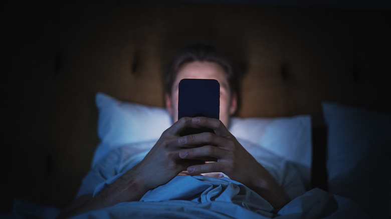 a man in bed illuminated by the blue light of the phone he is looking at
