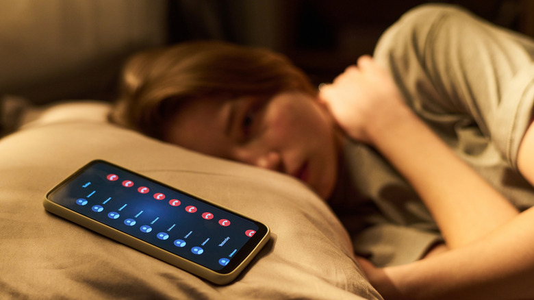 woman in bed at night with multiple notifications of calls on her phone