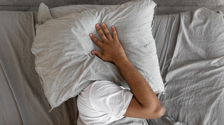 Man in covering his head with a pillow