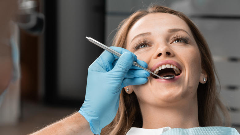 A dentist examines the teeth of a smiling patient.