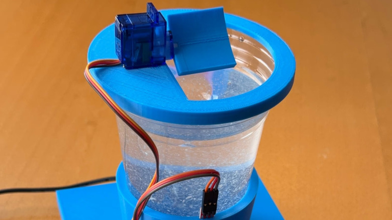 A fake drug detection device made of a cup of water with a blue base and half open lid. On top is a sensor with wires coming out.