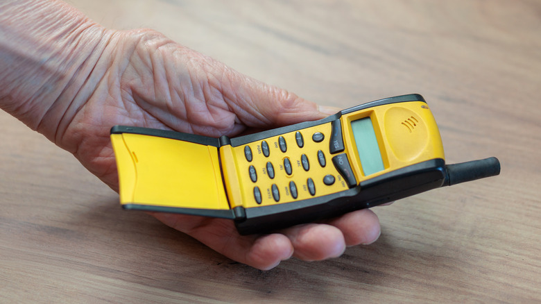 A hand holding an old yellow flip phone