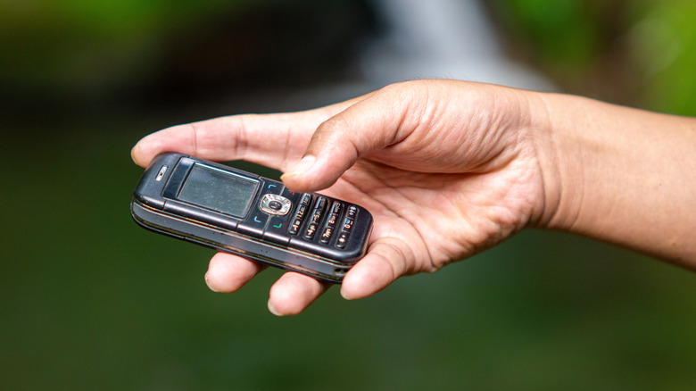 A hand holding a small, old cell phone with a numeric keypad.