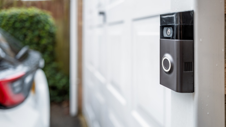 Close up of a video doorbell mounted next to a garage door with a vehicle in view.