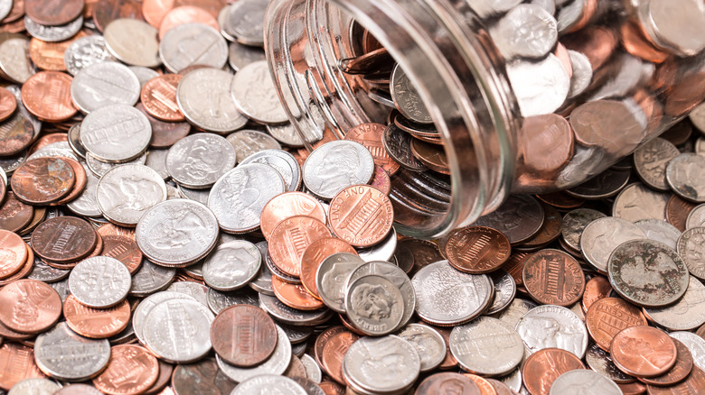A glass jar sitting atop a pile of U.S. coins of varying denominations