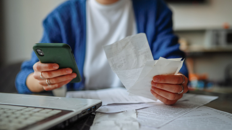 A closeup of a woman holding multiple receipts in one hand her cellphone in the other