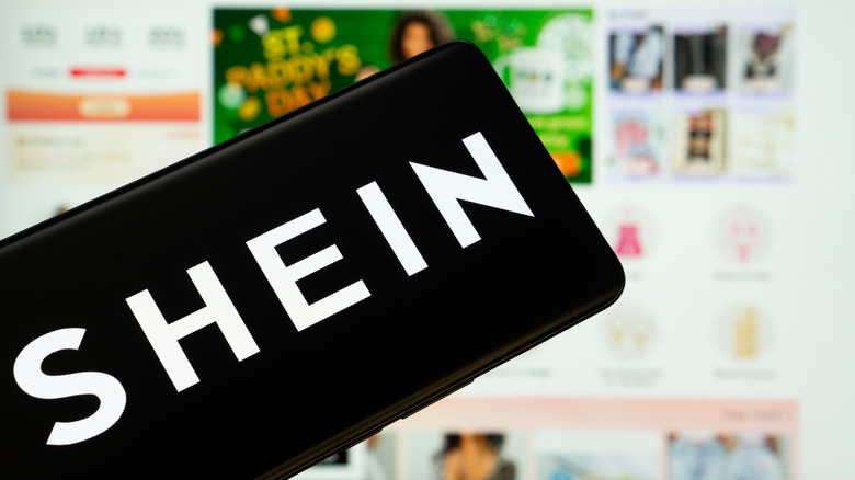the Shein logo on a smartphone with the website in the backdrop
