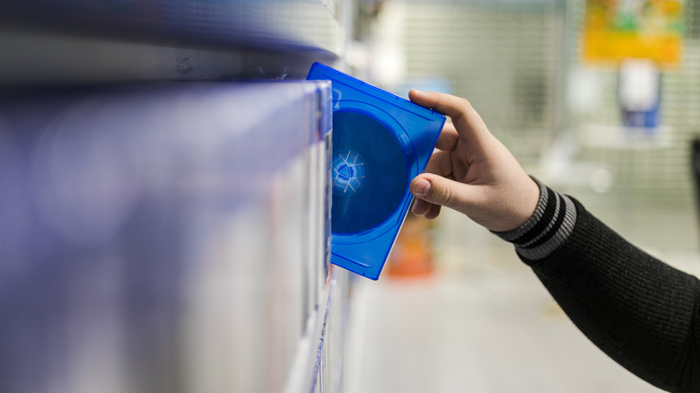 a hand grabbing a physical disc from a store shelf