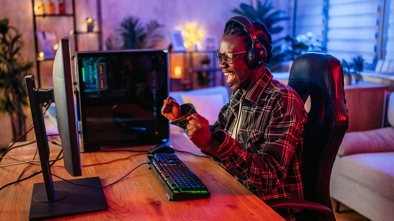 A person celebrating while sitting in front of a gaming computer and wearing headphones