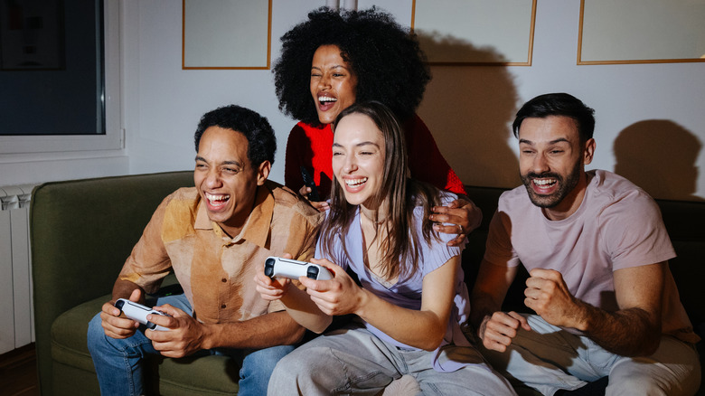 four people sitting on a couch with two holding PlayStation 5 controllers