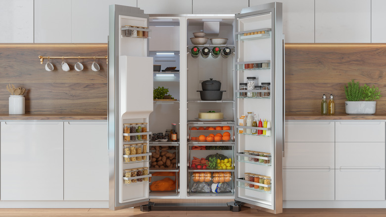 Modern refrigerator in the kitchen with doors open and groceries visible.