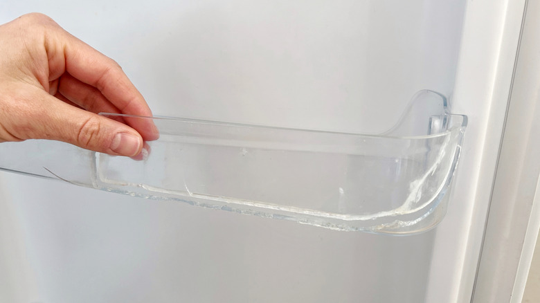 A hand holding a cracked and broken refrigerator shelf.