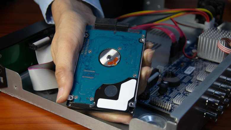 Someone holding a hard drive against an open mother board