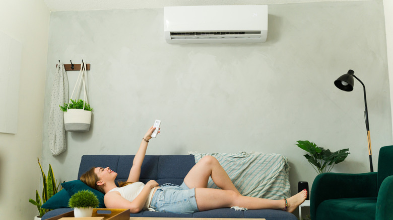 Person lying on a couch and using a remote control to control an air conditioning unit