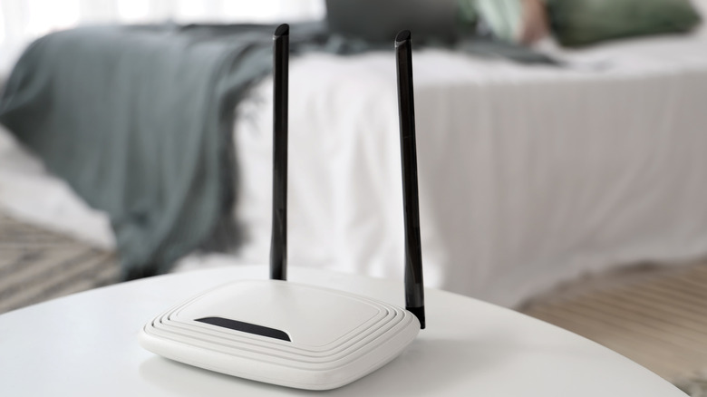 A router on a table with a bed in the background