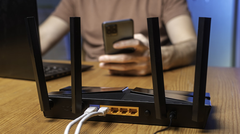 A Wi-Fi router on a desk with a person in the background using a smartphone and laptop