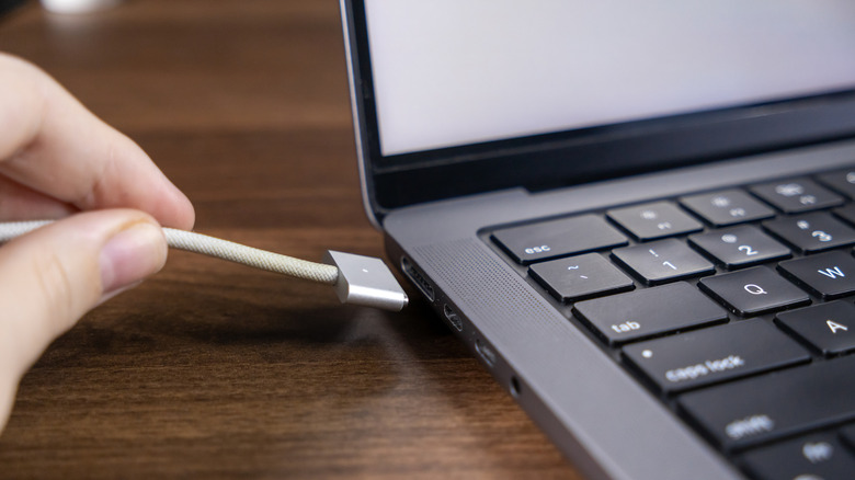 A MacBook user connecting the laptop to power via MagSafe.