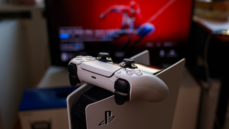 Dual Sense controller on PlayStation 5 console with Spider-Man onscreen in background.