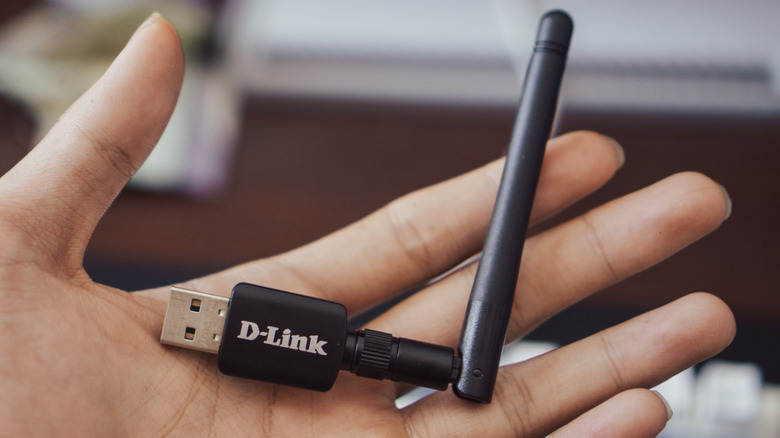 A USB Wi-Fi dongle with an antenna rests in a person's hand