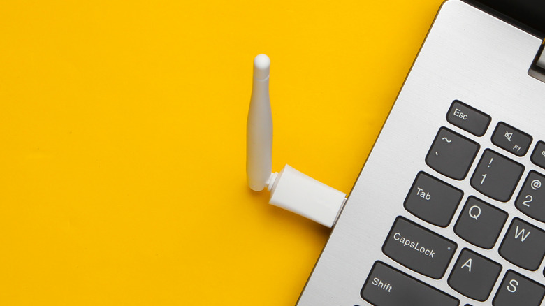 A USB Wi-Fi adapter plugged into a laptop on a bright yellow background