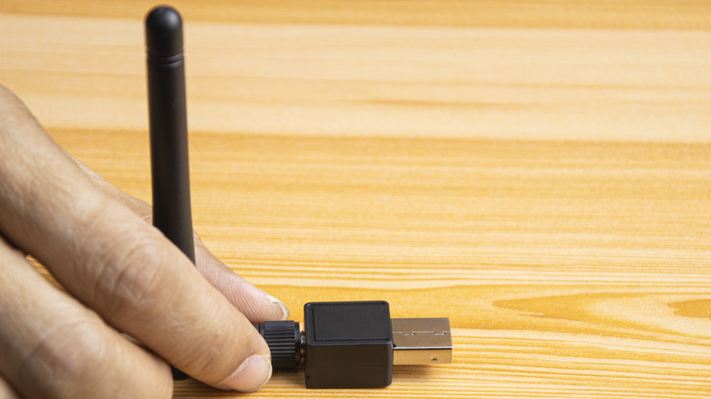 A USB Wi-Fi adapter held in hand above a wooden table