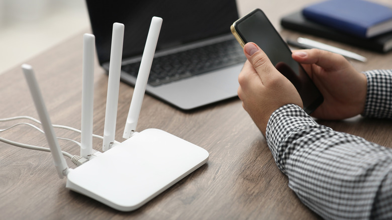 Person using a phone next to a laptop and Wi-Fi router