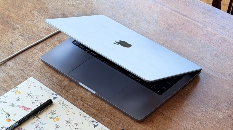 A MacBook Pro half closed on a desk alongside some flowery paper and a pen